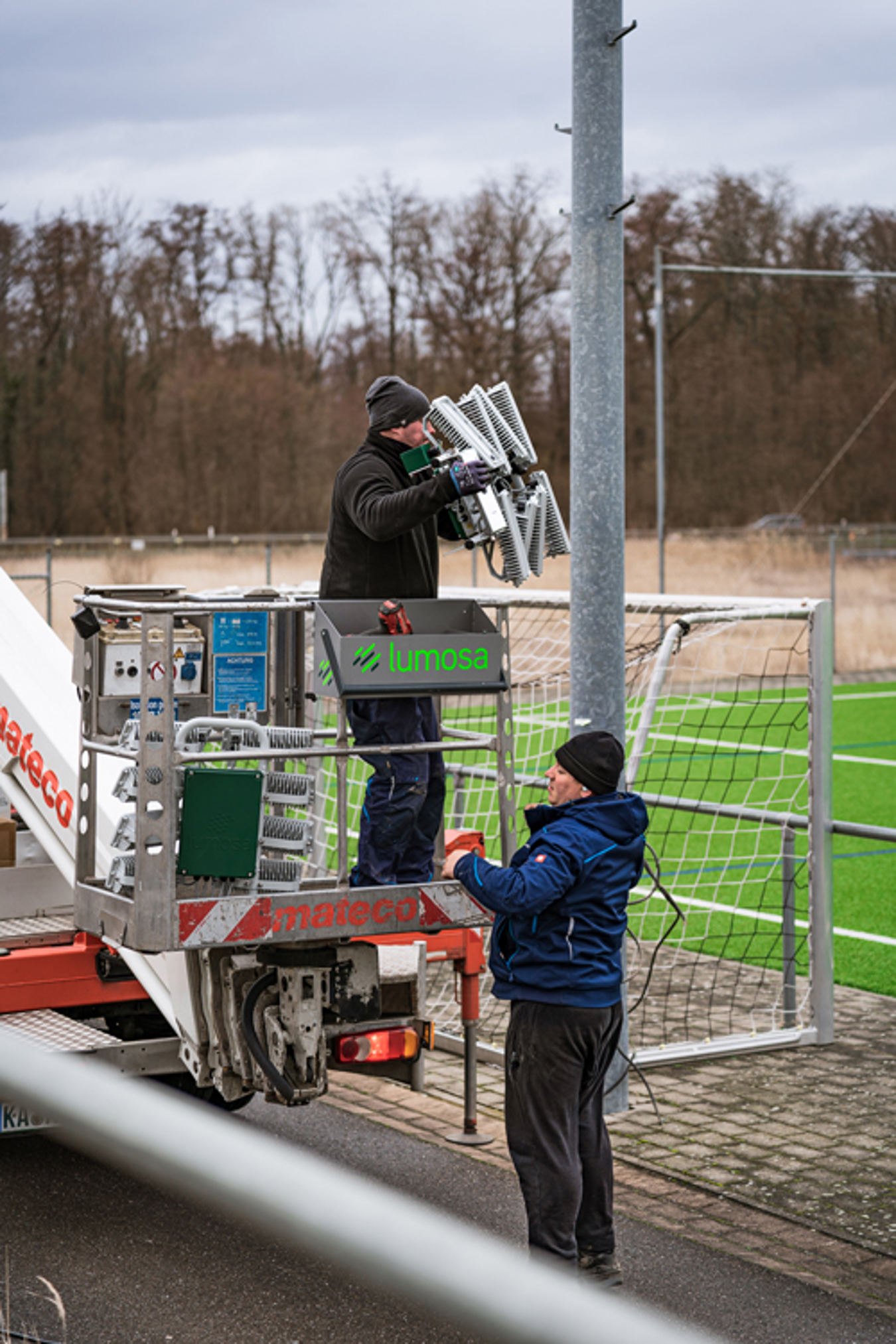Technician installing Lumosa retrofit LED sports lighting on existing football pitch masts at SV Gottenheim.