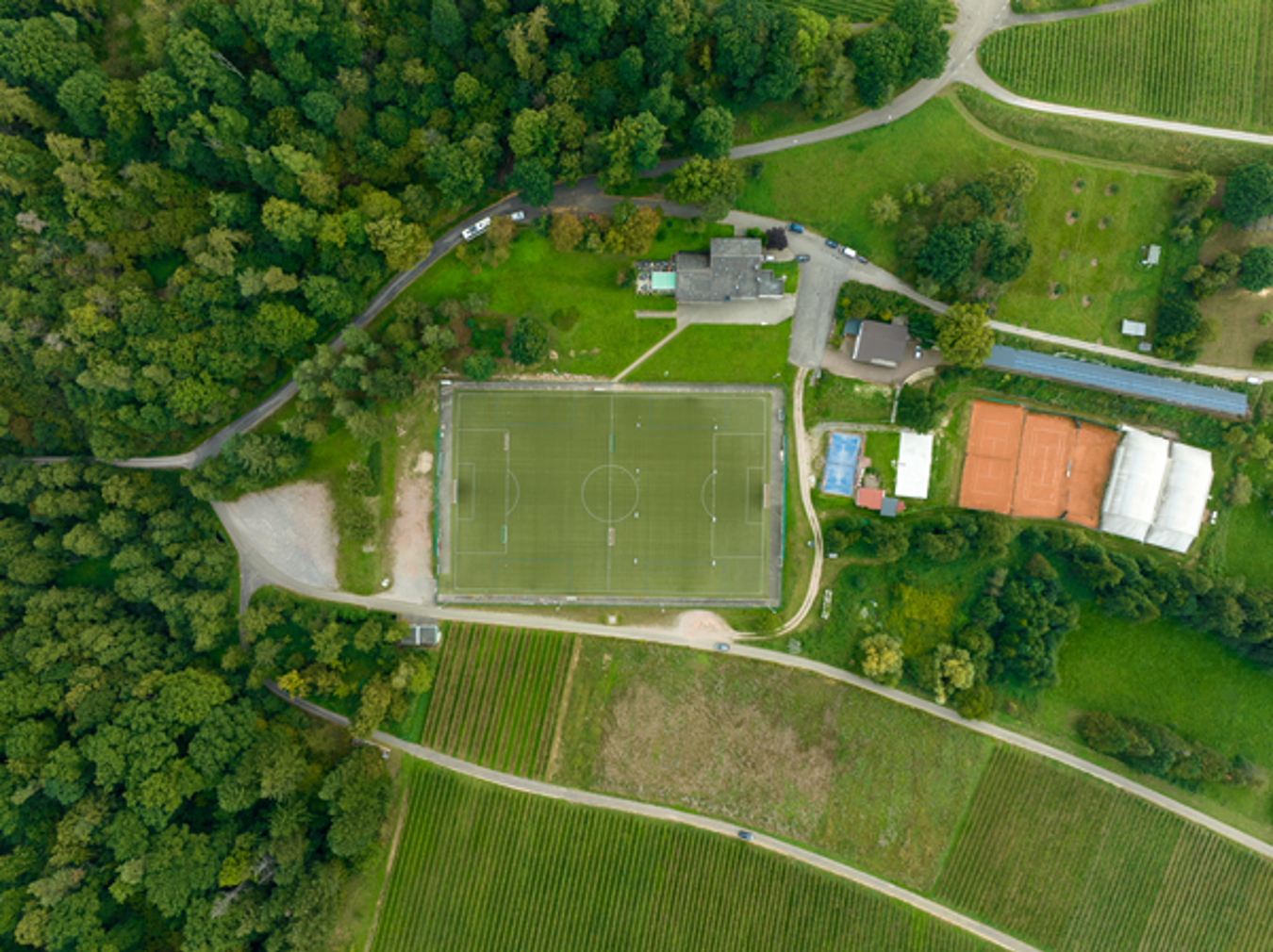 Aerial view of the FC Varnhalt football pitch surrounded by vineyards and woodland, illuminated with Lumosa LED sports lighting.