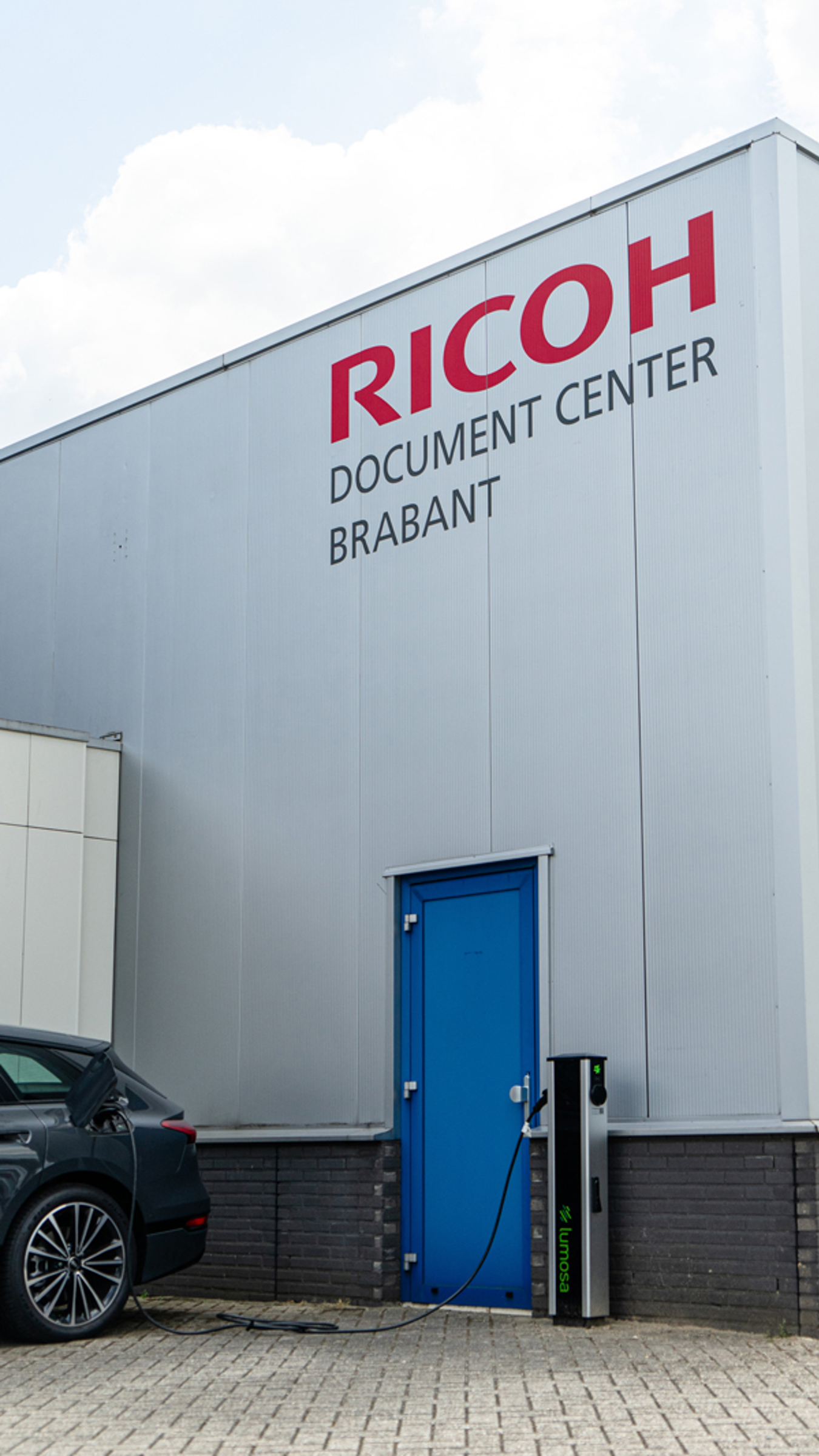 Elektrische auto geparkeerd naast een Lumosa TRACK laadpaal bij Ricoh Document Center Brabant in Eindhoven.