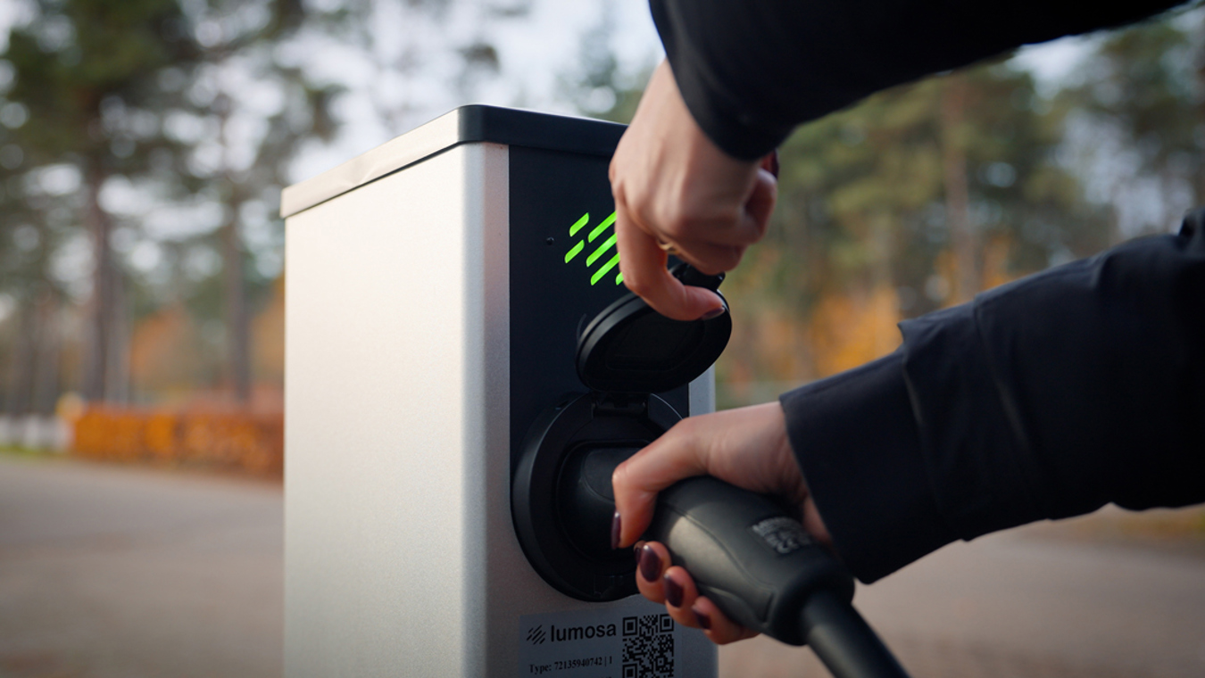 Hand sluit de laadstekker aan op een Lumosa TRACK laadpaal bij HC Tilburg om een elektrische auto op te laden.