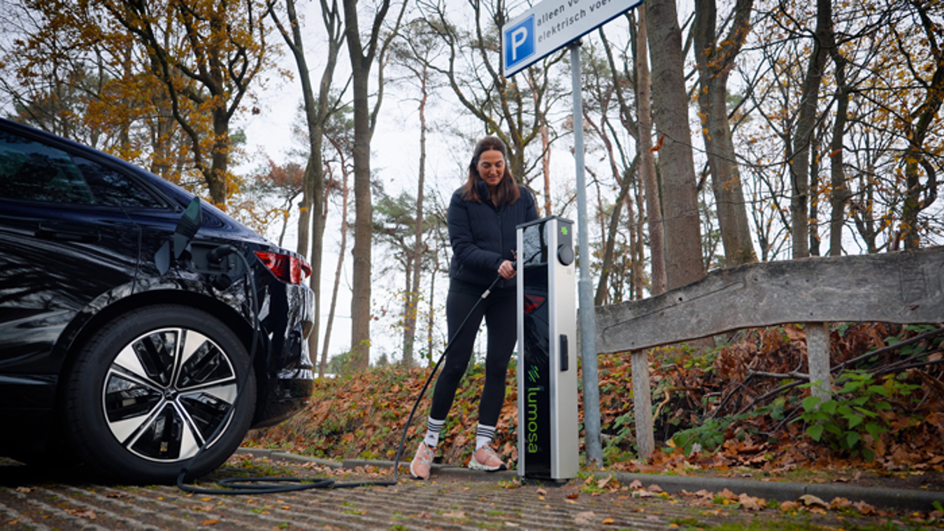Vrouw sluit haar elektrische auto aan op een Lumosa TRACK laadpaal bij HC Tilburg tijdens een bezoek aan de hockeyclub.