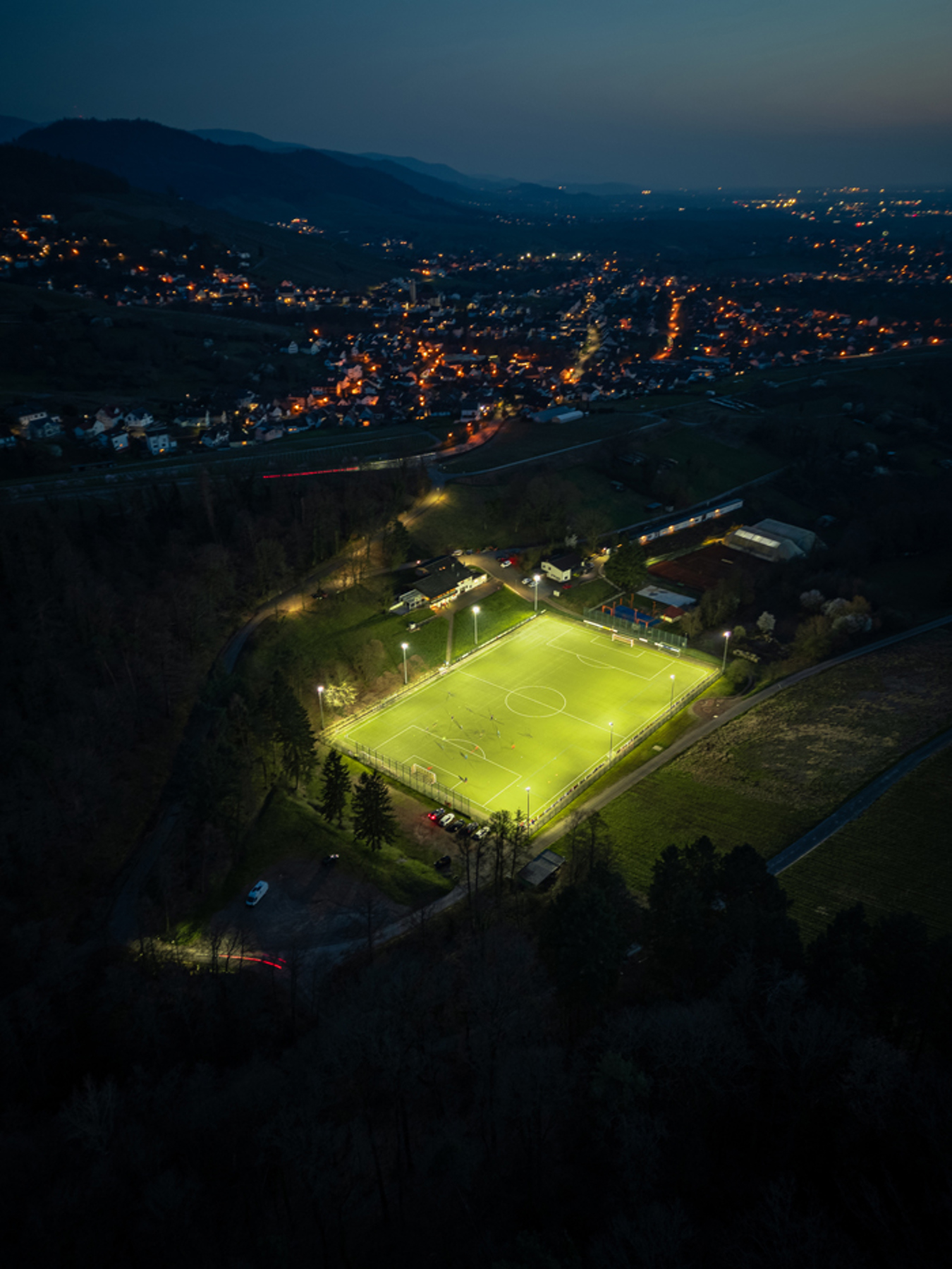 Aerial view of the FC Varnhalt football pitch illuminated by Lumosa LED sports lighting at dusk.
