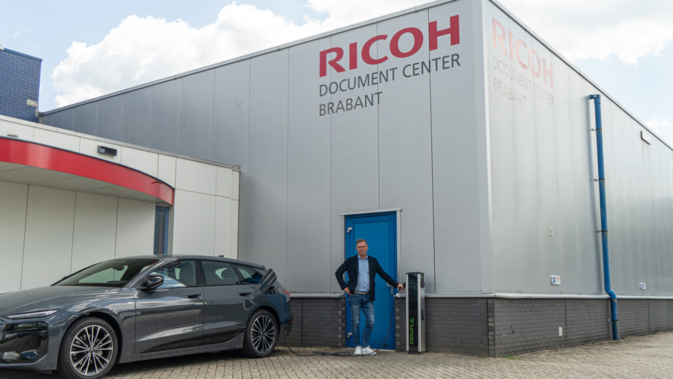 Jos de Greef van Ricoh Document Center Brabant staat bij een Lumosa TRACK laadpaal en een elektrische auto op de bedrijfslocatie in Eindhoven.