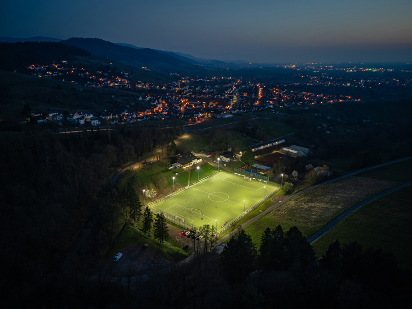 Aerial view of FC Varnhalt football pitch illuminated by Lumosa LED sports lighting during an evening match.